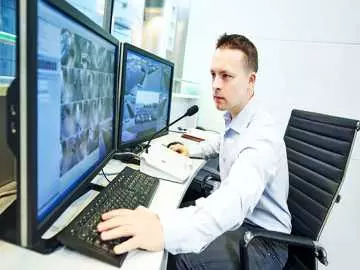A security guard watching a monitor with feeds of several security cameras